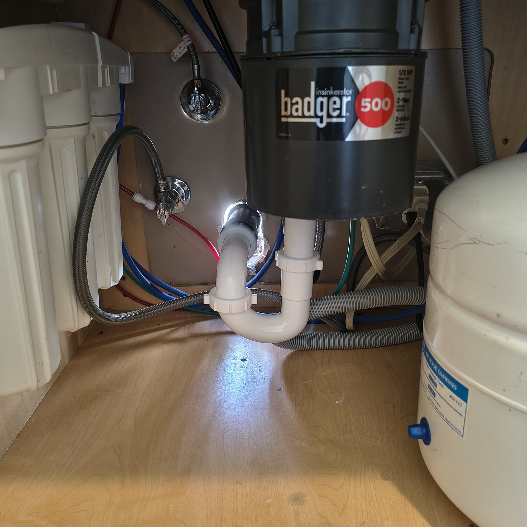 Reverse osmosis tank and plumbing beneath a kitchen sink